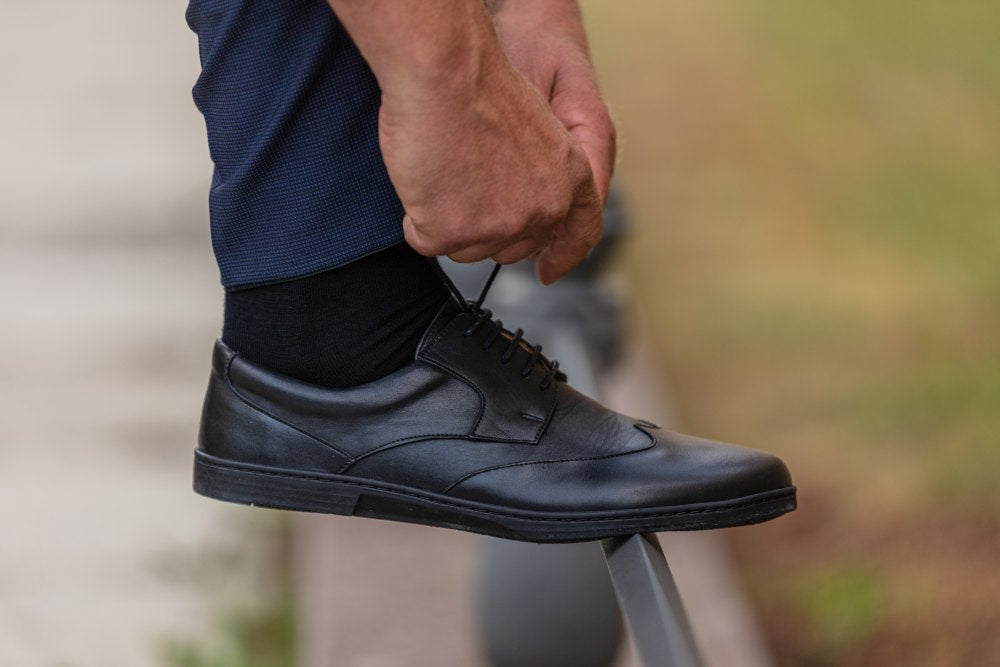 Ein Paar Oxford-Schuhe aus schwarzem Leder BRIQ Prime von ZAQQ mit Schnürung, bei der ein Schuh auf dem anderen vor einem weißen Hintergrund ruht. Diese eleganten Business-Schuhe strahlen Raffinesse aus und sind mit einer bequemen Barfußsohle für ganztägiges Tragen ausgestattet.