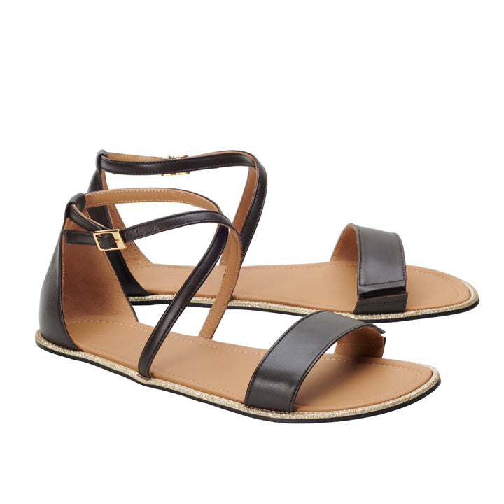 Die ZAQQ QEEP Dark Brown Sandalen mit dunkelbraunem Riemchendesign sind fachmännisch aus Nappaleder gefertigt. Sie verfügen über flache Sohlen und Knöchelriemen mit kleinen goldenen Schnallen, die außergewöhnlichen Tragekomfort gewährleisten. Vor einem weißen Hintergrund präsentiert, vereinen sie nahtlos Stil und Komfort.