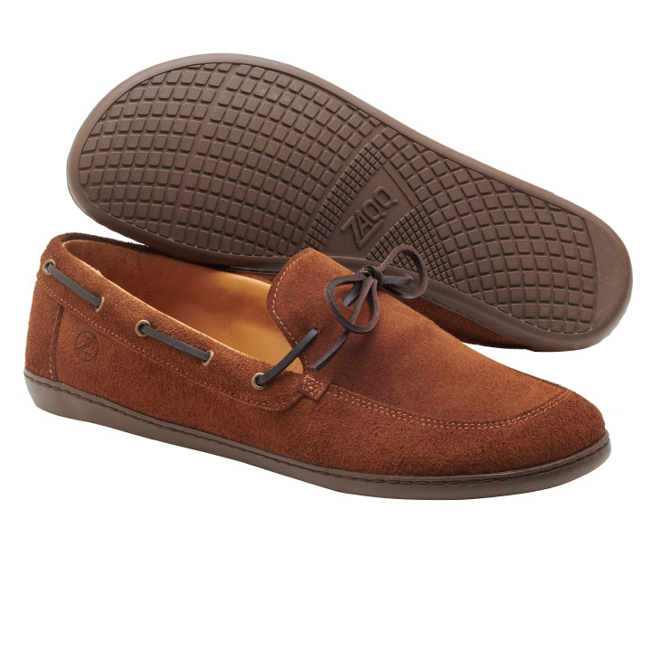 Der QEA Velours Cognac von ZAQQ unterstreicht mit seinem braunen Wildlederdesign, der Gummisohle und den dekorativen Schnürsenkeln einen eleganten Stil. Ein Schuh steht aufrecht, während der andere mit der strukturierten Sohle aufwartet und so wirklich die Essenz eines eleganteren Herrenschuhs verkörpert.