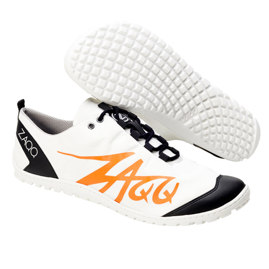 Die SQIM White Orange Schuhe von ZAQQ sind aus veganem Recyclingstoff gefertigt und zeichnen sich durch ein weißes, sportliches Design mit schwarzen und orangefarbenen Akzenten aus. Der Barfußschuh hat eine Sohle mit Gittermuster, schwarze Schnürsenkel und trägt den Markennamen ZAQQ in großen orangefarbenen Buchstaben auf der Seite.