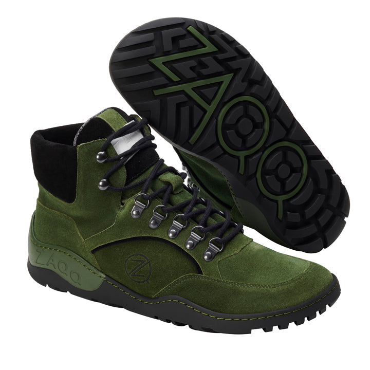 Abgebildet ist ein Paar ZAQQ TREQ Green Waterproof Wanderstiefel. Ein Stiefel ist aufrecht dargestellt, was sein Schnürdesign vorne und an der Seite betont, während der andere geneigt ist, um die schwarz-grüne ZAQQ TERRA-Profilsohle zu präsentieren. Der obere Teil besteht aus Wildleder und Textilmaterialien und trägt zu einem robusten Outdoor-Look bei.