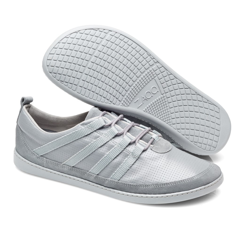 Die SPARQ Low Grey Sneaker von ZAQQ zeichnen sich durch ein elegantes, modernes Design aus Nappaleder aus. Ein Schuh liegt flach, um das perforierte Obermaterial und die Schnürung zu präsentieren, während der andere hochgestellt ist, um die strukturierte Kautschuksohle hervorzuheben.