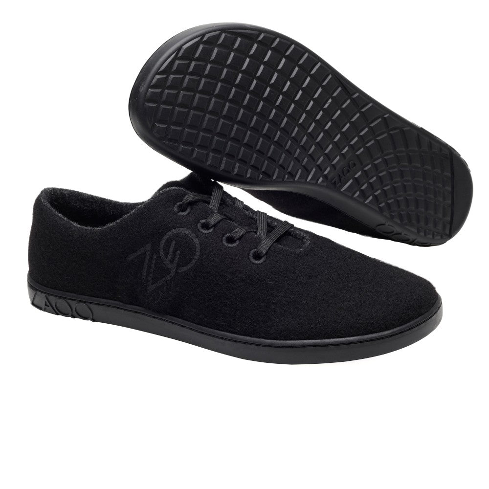 Die LIQE Black Sneaker von ZAQQ zeichnen sich durch ein elegantes Design mit schwarzer Schnürung, strukturierten Sohlen und einem dezenten Logo aus. Vor einem schlichten weißen Hintergrund steht ein Schuh aufrecht, während der andere sich neigt und sein Merinowollfutter für eine natürliche Temperaturregulierung freigibt.