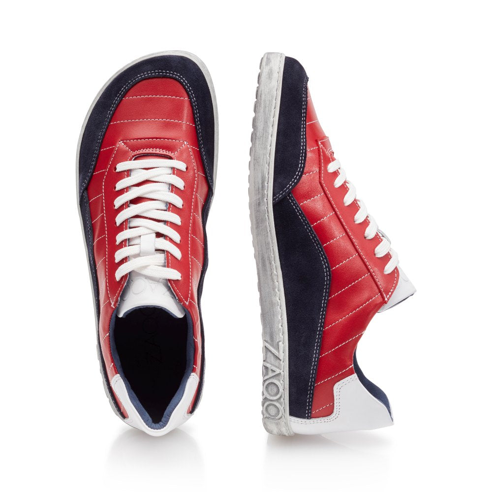 Zwei QAMPION Navy Red Sneaker von ZAQQ sind mit rotem Nappaleder, blauem Wildleder und weißen Akzenten versehen. Ein Schuh ist von oben abgebildet, während der andere von der Seite gezeigt wird, was die weißen Schnürsenkel und eine strukturierte graue Sohle hervorhebt.