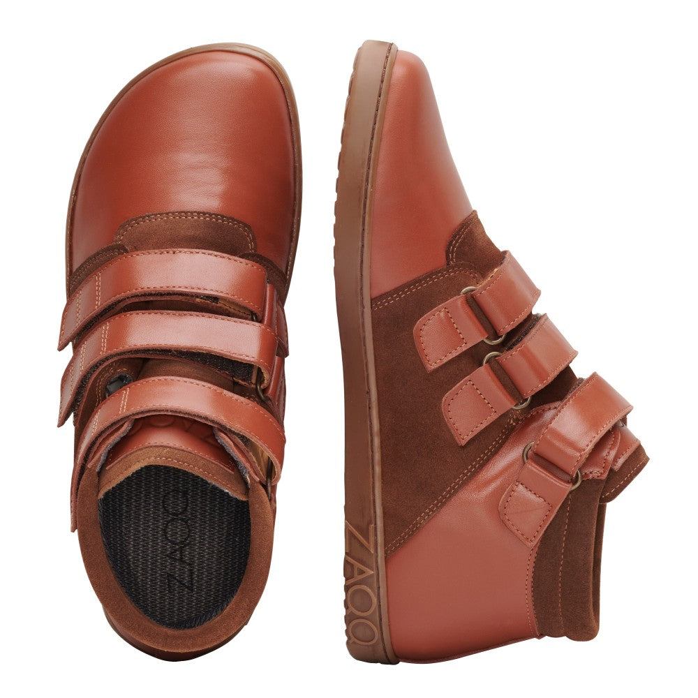 Der QOOPER Cognac von ZAQQ ist ein Paar braune Lederschuhe mit Klettverschluss und aus hochwertigem Nappaleder gefertigt. Ein Schuh ist von oben zu sehen, der andere von der Seite. Beide zeigen eine leicht strukturierte Sohle mit dem Markenlogo auf einer Seite.