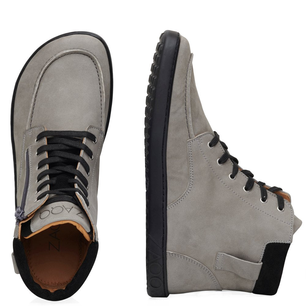 Ausgestellt wird ein Paar ROQA Grey High-Top-Sneaker von ZAQQ, mit einem grauen Design mit schwarzen Sohlen und Schnürsenkeln. Ein Schuh ist von oben zu sehen, der andere steht aufrecht und zeigt sein Seitenprofil. Diese halbhohen Sneakers verfügen über ein dezentes Reißverschlussdetail und ein Branding auf der Zunge, was für flexibleren Tragekomfort sorgt.