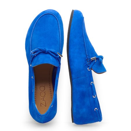 Die FLIQ Blue von ZAQQ sind hellblaue Mokassin-Loafer aus Wildleder mit Schnürsenkeln, von oben und von der Seite zu sehen. Diese Schuhe aus Veloursleder haben eine hellbraune Innenseite mit ZAQQ-Branding und eine schwarze Sohle und vereinen traditionellen Stil mit modernem Komfort.