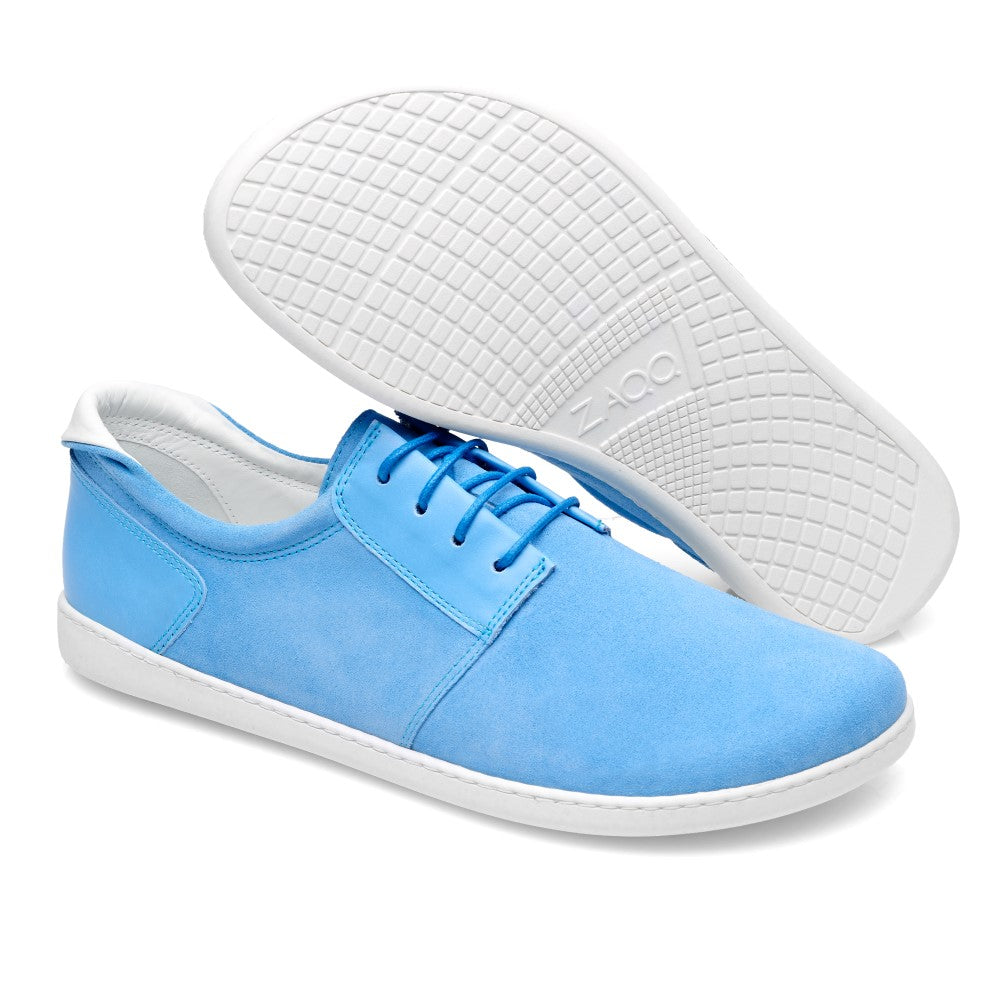 Präsentiert wird ein Paar PIQUANT Pool-Sneaker von ZAQQ, die eine stilvolle Mischung aus lässigen blauen und weißen Sohlen auf einem sauberen weißen Hintergrund präsentieren. Ein Schuh liegt flach, während der andere sich neigt und seine markante Sohle mit Gittermuster zeigt. Das Schnürdesign aus hochwertigem Veloursleder verbindet auf elegante Weise Stil und Komfort.