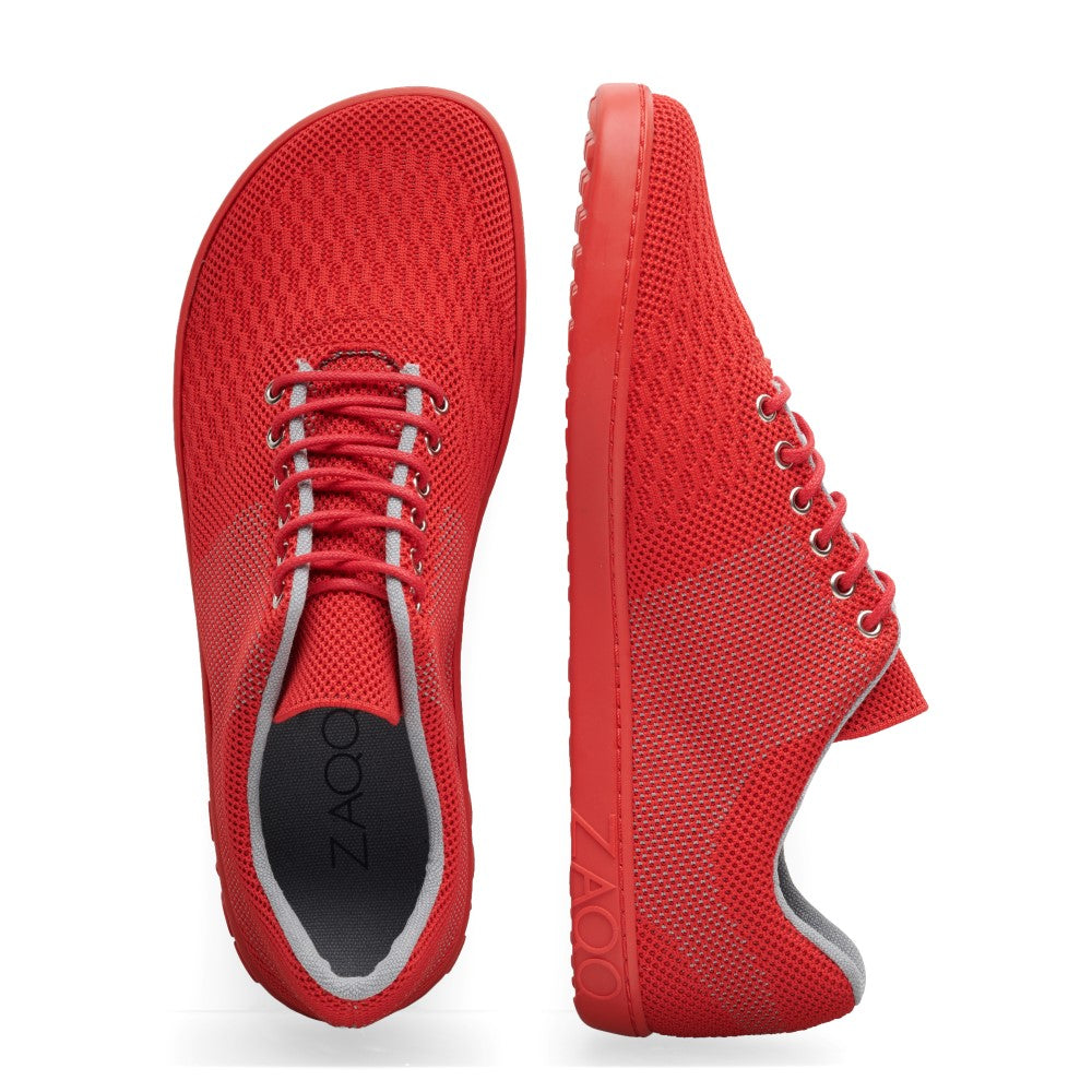 Die QNIT Red von ZAQQ sind leuchtend rote Freizeit-Sneaker mit atmungsaktivem Mesh-Obermaterial und grauem Innenfutter. Ein Schuh wird von oben mit ordentlich gebundenen Schnürsenkeln gezeigt, während der andere im Seitenprofil gezeigt wird, wodurch die Sohle und die Strickgewebe-Textur hervorgehoben werden. Diese Schuhe sind perfekt für alle, die nach stylischen veganen Sneaker-Optionen suchen.