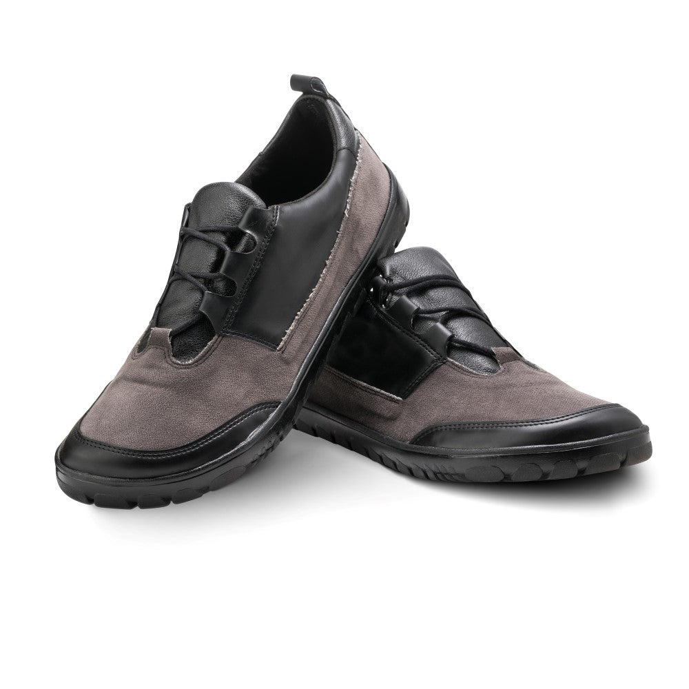 Der QUEST Low Black Waterproof von ZAQQ ist ein Paar stylischer Outdoor-Schuh für Herren in grau-schwarzem Design. Diese Schuhe bestehen aus einer Kombination aus Wildleder und Leder und sind mit schwarzen Schnürsenkeln versehen. Sie sind wasserdicht. Sie werden so präsentiert, dass ein Schuh aufrecht steht, während der andere dagegen lehnt.